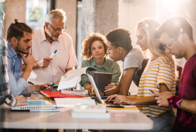 A college professor teaches a group of five students gathered around a table.